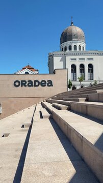 Town name sign reading Oradea beside a staircase with Zion Neolog Synagogue visible in the background in Oradea, Romania. Vertical travel footage.