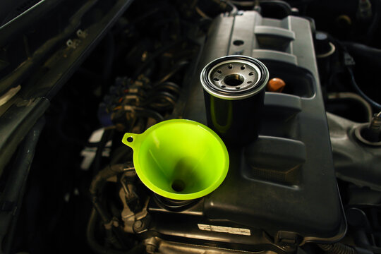 Bright green funnel and new black oil filter placed on a car engine during an automotive routine oil change service