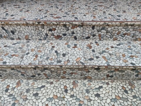 a set of outdoor tiled steps or stairs decorated with a highly detailed, textured pattern that closely mimics natural, rounded river stones or pebbles