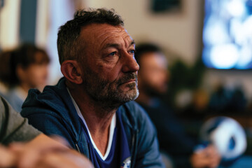 Obraz premium A mature man with a thoughtful expression gazes off into the distance, engaged in deep reflection while surrounded by others, suggesting a shared experience.