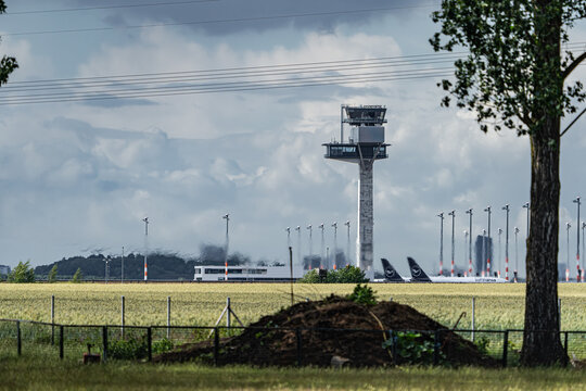 Berlin, Berlin, Germany - 13 June 2026: View of the control tower and parked aircraft at the ILA Berlin Air Show with a grassy field in the foreground under a cloudy sky.