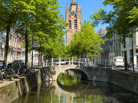 Leaning old church Oude Kerk Gothic tower above canal bridge on sunny day in Delft City Centre, Netherlands