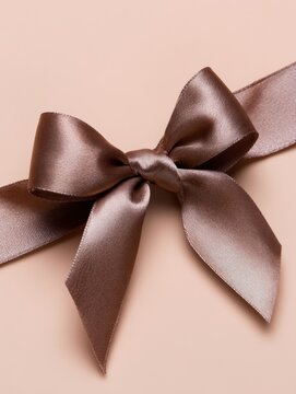 Elegant brown satin ribbon bow with smooth shimmering texture on a warm tan background for gift packaging and celebration design
