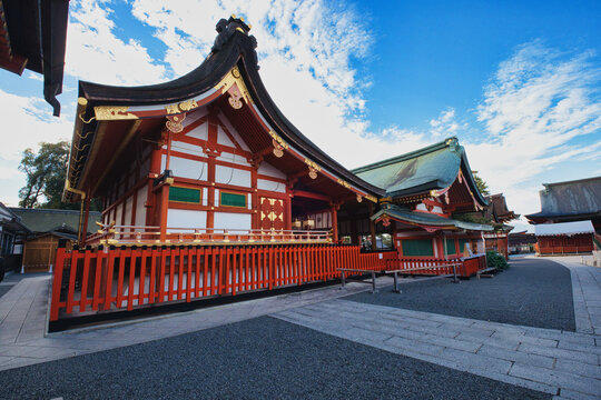 Kyoto, Kyoto, Japan - 12 November 2025: View of Fushimi Inari Taisha with its iconic vermilion wooden architecture, intricate gold detailing, and stone pathways under a bright blue sky.