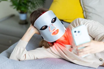 Woman relaxing with LED facial mask and smartphone © Алина Бузунова