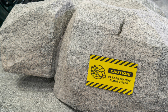 Large artificial boulders displayed indoors with a yellow caution sign warning visitors not to climb or step on the decorative rock installation. 