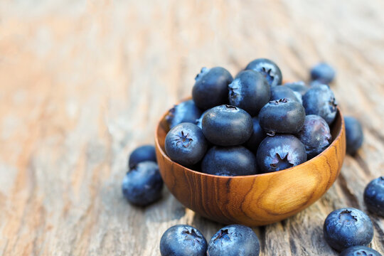 Fresh blueberries in a small wooden bowl on rustic wooden background with copy space.