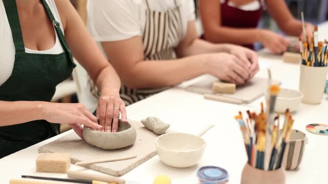 Girls hands forms bowl of clay during master class, close up. Unrecognizable people team of creative enthusiasts is engaged in clay modeling lesson.