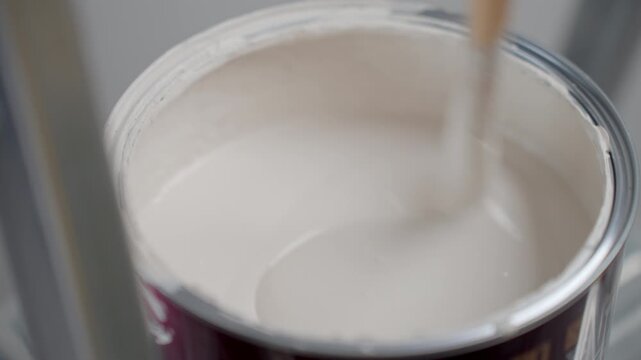 Process of stirring white paint in an open paint can with a wooden stick. Concept of painting preparation renovation and DIY repair.