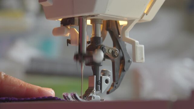 Mature hands guide fabric at sewing machine as needle moves up and down during garment construction, close up