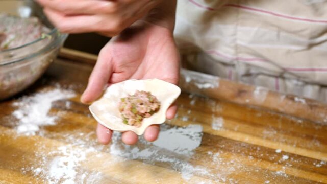 Hands shaping dumpling wrapper on floured wooden table