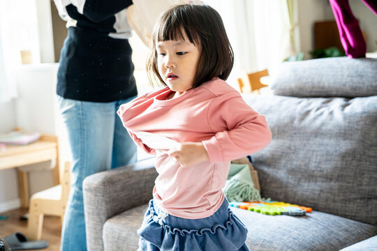 Independent little Asian girl changing clothes and putting on a pink shirt by herself
