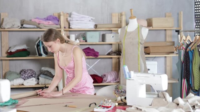 Young woman tailor drawing with pencil on brown paper, she sketching clothes and patterns on table in sewing workshop. High quality 4k footage