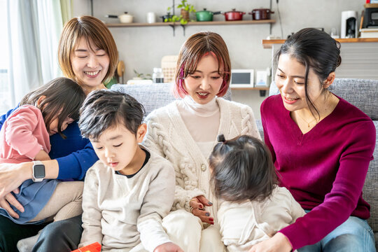 Joyful group of Asian mothers and young children laughing together during a lively gathering at home