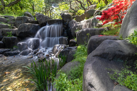 Long exposure of a beautiful small waterfall cascading over rocks in a lush green garden.