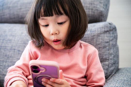 Close up of a surprised little Asian girl looking at a smartphone screen with an open mouth