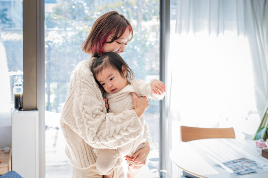 Loving Asian mother holding her sweet toddler affectionately in a bright sunlit room