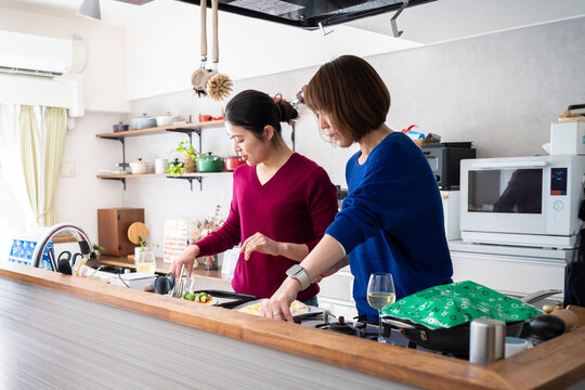 Two focused Asian women preparing homemade pizzas together at a modern kitchen counter