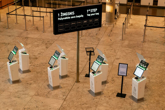 VILNIUS, LITHUANIA - JUNE 7, 2026: High angle view of self-service bag tag printing kiosks with a large digital information navigation screen at Vilnius International Airport