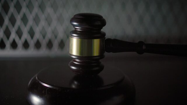 A judge's gavel resting on a sound block photographed against a dark blurred background with a subtle diamond pattern texture.