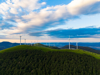 Obraz premium Wind turbines stand on a green hill under a cloudy sky in a rural area during late afternoon