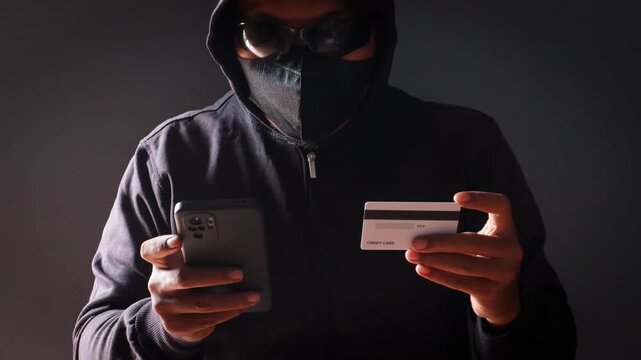 Anonymous cybercriminal using a smartphone and credit card in a dark environment, representing online fraud, phishing attacks, identity theft, financial scams, and cybersecurity threats.
