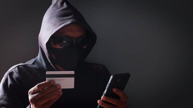 Anonymous cybercriminal using a smartphone and credit card in a dark environment, representing online fraud, phishing attacks, identity theft, financial scams, and cybersecurity threats.