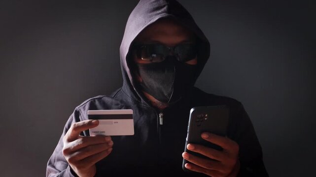 Anonymous cybercriminal using a smartphone and credit card in a dark environment, representing online fraud, phishing attacks, identity theft, financial scams, and cybersecurity threats.