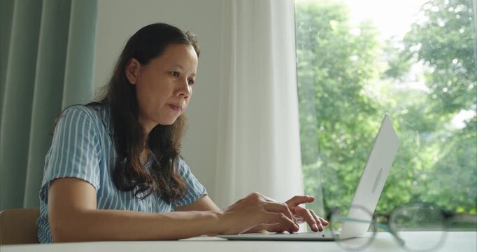 Asian middle woman  typing work on computer, women using working with laptop at home office. Side view