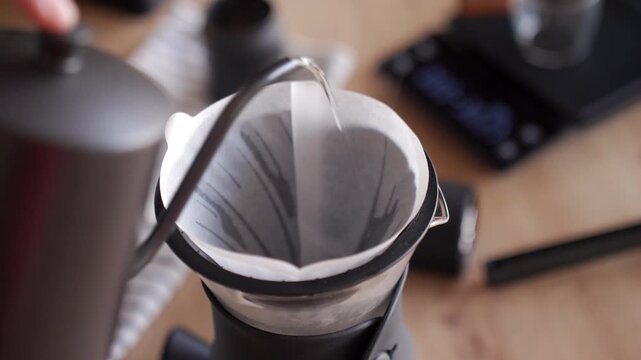 Warming paper filter with hot water in a coffee dripper before brewing. Process of preparing specialty drip coffee with pour over method