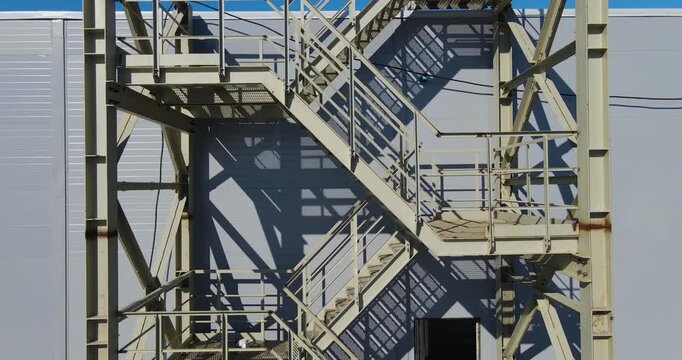 Aerial ascending close-up shot of an external steel fire escape staircase on the facade of a modern industrial building