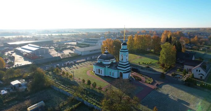 Cinematic aerial circling shot of a rural Orthodox church revealing an agricultural facility and autumn landscapes in the background