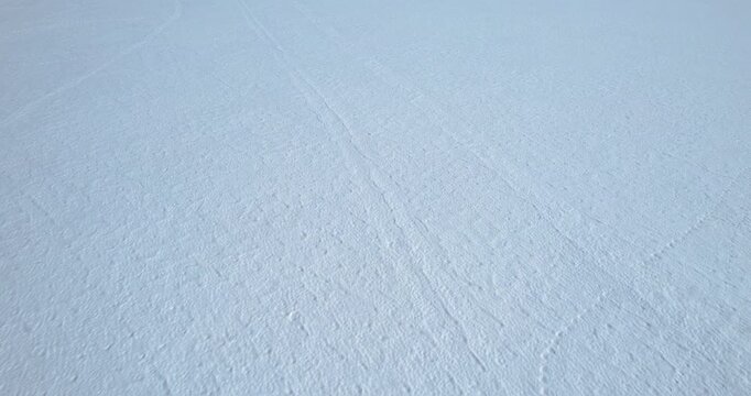 Top-down aerial shot of an animal trail traversing a snowy field with patches of exposed ground and ice