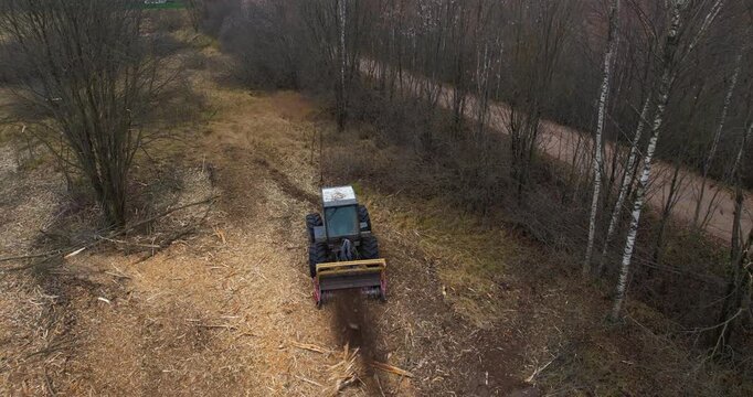 Aerial high-angle shot looking down at a forestry mulching machine cutting a fresh path through dense brush and trees