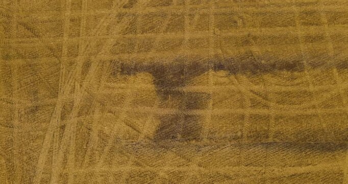 Top-down aerial texture shot directly above a golden harvested agricultural field covered in chaotic tire tracks and machinery trails