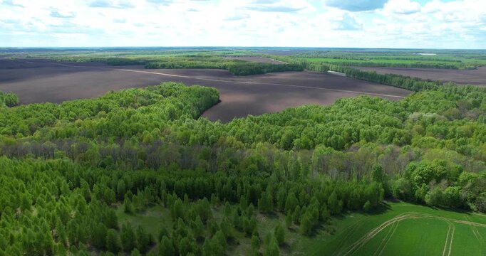 High angle aerial panorama of a scenic patchwork landscape with dark plowed fields, green crops, and fresh spring forests