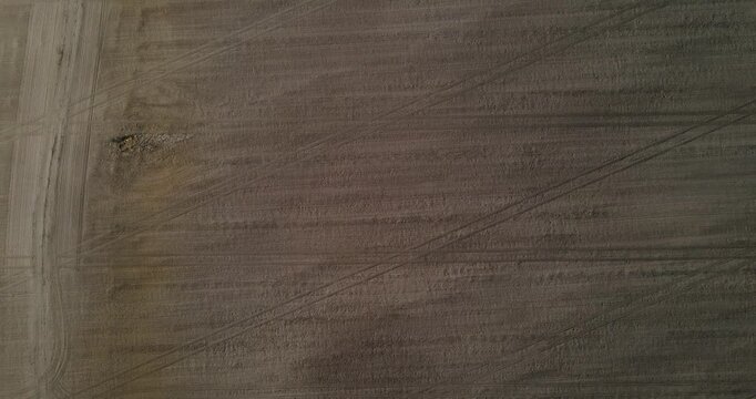 Top-down aerial view of intersecting tractor tire tracks patterned on a dark plowed agricultural dirt field