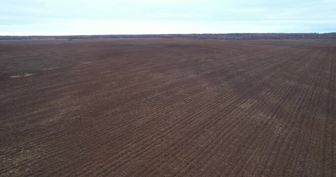 Aerial forward flying wide shot over expansive dormant agricultural fields and patches of forest in the rural countryside