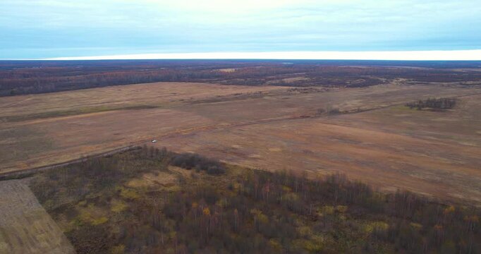 Aerial forward flying wide shot over expansive dormant agricultural fields and patches of forest in the rural countryside