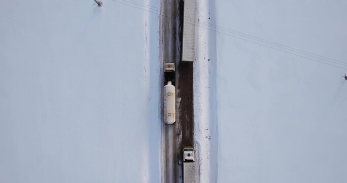 Top-down aerial view directly above heavy freight trucks driving on a snowy winter road surrounded by a vast white field