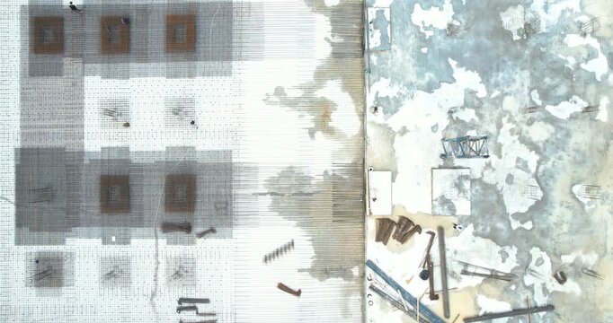 Aerial top-down tracking shot moving along a construction site showing a massive rebar grid foundation and a wooden retaining wall