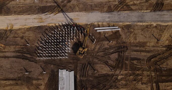 Aerial descending top-down view of a heavy pile driving machine installing concrete pillars into the dirt foundation