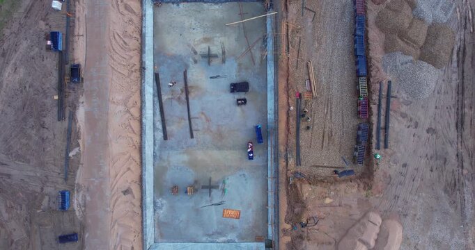 Top-down aerial shot of a large concrete foundation pit with exposed rebar and sand piles at a construction site
