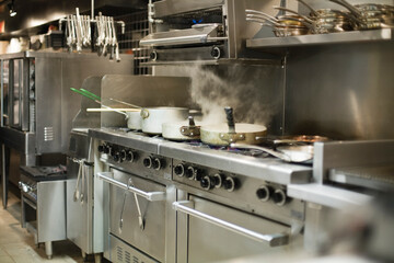 Naklejka premium Stainless steel commercial kitchen with pots and pans steaming on the
