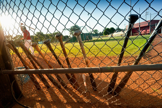 View through a chain link fence of baseball bats in a dugout with a