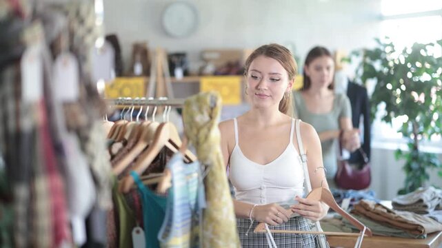 Young woman customer making choice and elect something summer clothing in store, and buyer consider some items. Modern urban fashion, casual practical clothes made of natural fabrics