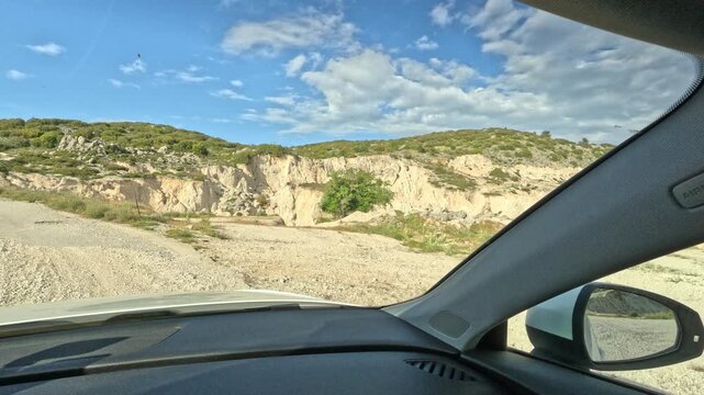 Point-of-view drive through a rugged quarry and white rock landscape on Lefkada Island, Greece. The footage captures a remote gravel road surrounded by exposed limestone cliffs, rocky terrain