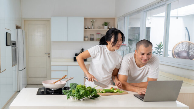 Young Couple Using Laptop While Cooking Healthy Recipe Together in Kitchen