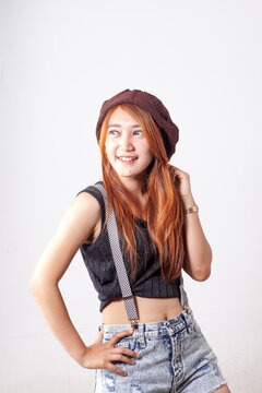 Trendy Young Asian Woman in Beanie and Suspenders Posing against White Background