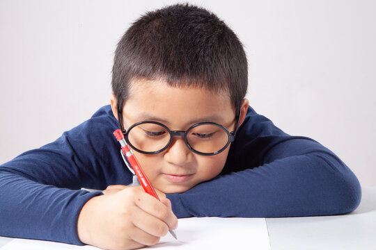 Focused Young Asian Boy with Glasses Writing on Paper with Pencil